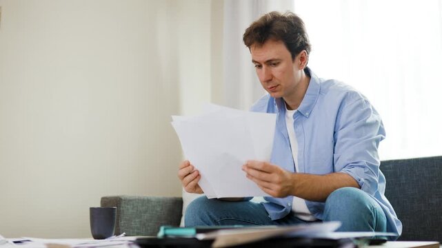 Stressed man reviews high utility bills, household expenses and costs. Overwhelmed by financial crisis, inflation and unpaid debts, he covers his face in extreme economic pressure. 4k footage