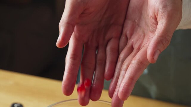 Fresh Pomegranate Arils Falling from Hands into a Glass Bowl