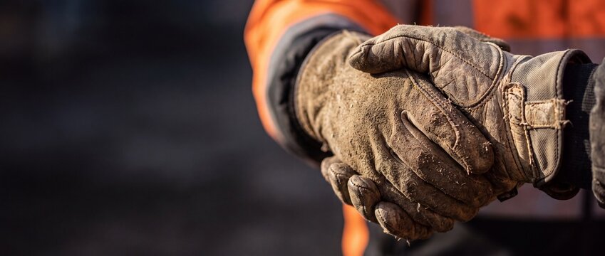 Close up of two industrial workers wearing dirty protective leather gloves shaking hands in agreement at an outdoor construction site with copy space
