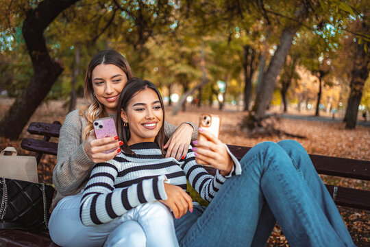 Two girls share a joyful moment in an autumn park while taking selfies