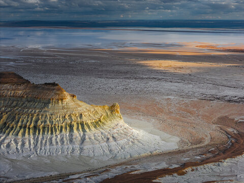 Aerial view of the dramatic Bozjyra rock formations rising from the vast salt flats and desert landscape under a cloudy sky in Aktau, Mangystau Region, Kazakhstan.