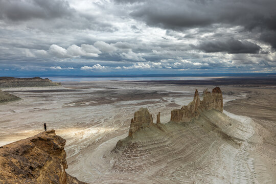 Aerial view of the dramatic limestone rock formations of Bozjyra under a cloudy sky with a person standing on a cliff edge in Aktau, Mangystau Region, Kazakhstan.