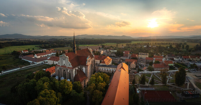 Aerial view of the Church of the Assumption and historic abbey surrounded by red-roofed buildings and green fields in the golden hour light in Kamieniec Zabkowicki, Lower Silesia, Poland.
