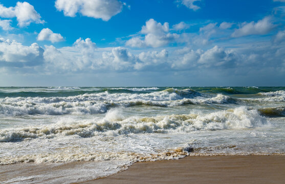 Energetic North Sea surf rolls onto the sandy beach between Westerland and Wenningstedt on Sylt beneath a vivid blue sky with towering summer clouds.