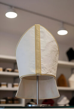 Religion and catholic tradition, white mitre of a bishop on a display stand in a church vestment shop with blurred shelves in the background