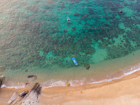 Aerial top view of pristine tropical beach with crystal clear turquoise water, coral reef, rocks, and small boats. Summer vacation and travel concept. Human-created, not AI.