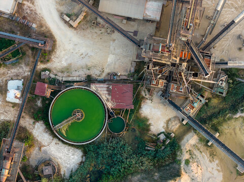Aerial view of an industrial facility featuring circular green water treatment tanks, complex conveyor belt systems, and processing structures in Rome, Lazio, Italy.