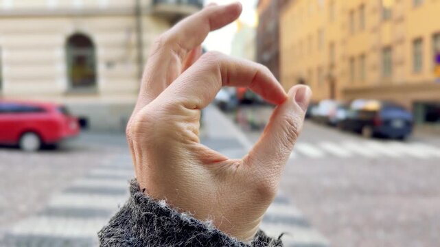 Hand Making an OK Gesture Against a Blurred Kruununhaka Helsinki City Street