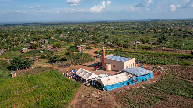Aerial view of the Bidibidi Refugee Settlement featuring a mosque, temporary shelters, and tents with people gathered in a rural landscape in Yumbe, Northern Region, Uganda.