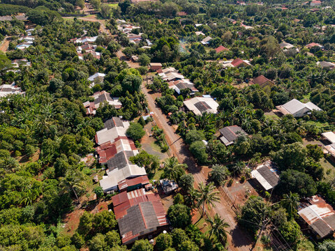 Aerial view of Chup Rubber Plantation featuring rows of rubber trees, rural houses with metal roofs, and a dirt road in Tbong Khmum, Tboung Khmum, Cambodia.
