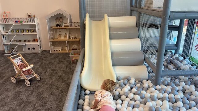 A girl slides headfirst on her stomach into a pit of white and blue balls, indoor recreation, active childhood, playful adventure.