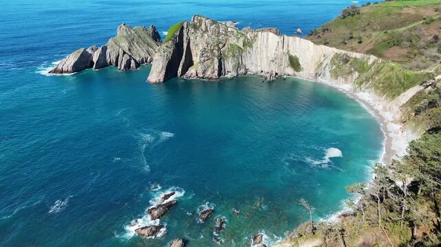 Camera moving up aerial view of curved beach with vertical rock strata cliffs and turquoise sea   