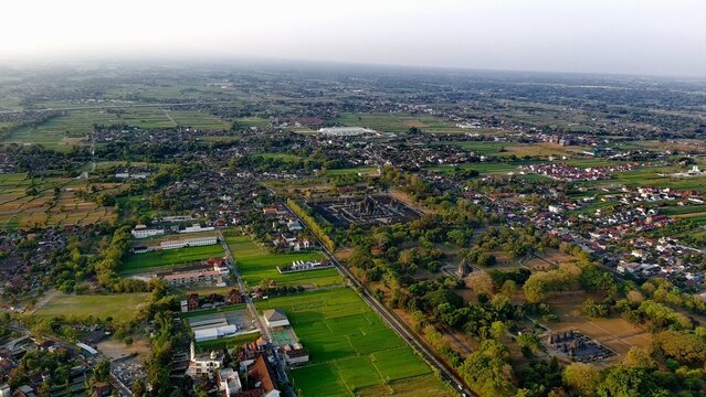 Aerial view of the historic Prambanan Temple complex surrounded by lush green rice fields, rural villages, and tropical vegetation in Prambanan, Central Java, Indonesia.