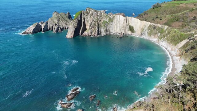 Aerial drone view of a curved beach with vertical rock strata cliffs and turquoise sea   