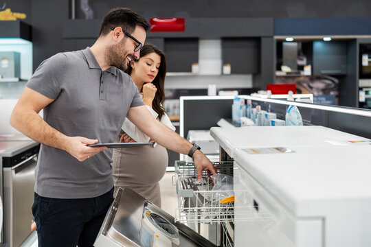 Retail assistant showing home appliances to an expecting customer, guiding her purchase decision in a modern showroom environment.