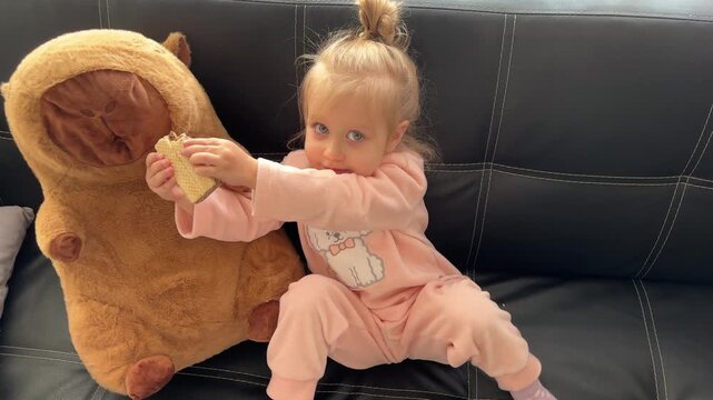A girl offers a wafer to her plush capybara and then eats it in a downward view, pretend play, childhood imagination, snack time.