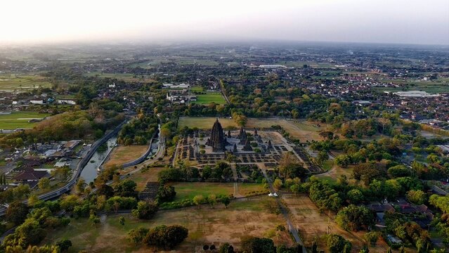 Aerial view of Prambanan Temple surrounded by lush greenery, ancient stone structures, and nearby residential areas in Kecamatan Prambanan, Daerah Istimewa Yogya, Indonesia.