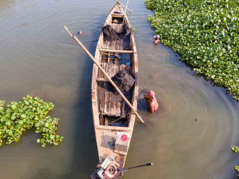 Aerial view of Kalirajut with fishermen working in a wooden boat surrounded by water hyacinths in a river in Patikraja, Central Java, Indonesia.