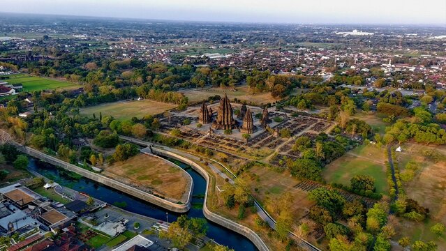 Aerial view of Prambanan Temple surrounded by lush greenery, ancient stone structures, and a winding river in the rural landscape, Kecamatan Prambanan, Daerah Istimewa Yogya, Indonesia.