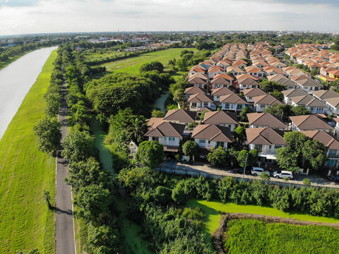 Top down drone view of modern suburban housing development with residential roofs near a canal and lush green trees. Real estate and property concept. Human-created, not AI.