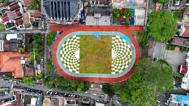 Aerial view of Taman Kota Lapang Merdeka Sukabumi featuring a checkered field surrounded by a running track and trees in the city center of Sukabumi, West Java, Indonesia.