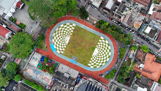 Aerial view of Taman Kota Lapang Merdeka Sukabumi featuring a checkered field, red running track, lush trees, and urban infrastructure in Sukabumi, West Java, Indonesia.