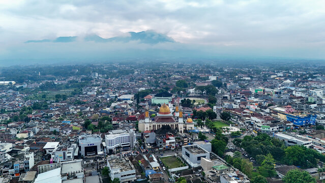 Aerial view of Masjid Agung Kota Sukabumi surrounded by the dense urban landscape with distant mountains under a cloudy sky in Sukabumi, West Java, Indonesia.