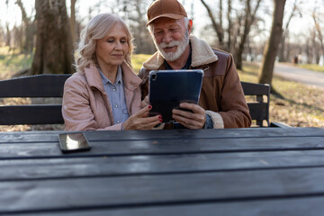 Elderly man and woman exploring a digital tablet together in a peaceful park, illustrating digital literacy, lifelong learning and technology adoption among seniors © lordn