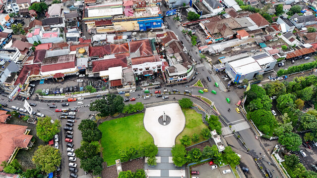 Aerial view of the city square featuring a central monument, surrounding urban buildings, busy streets with traffic, and lush green trees in Sukabumi, West Java, Indonesia.