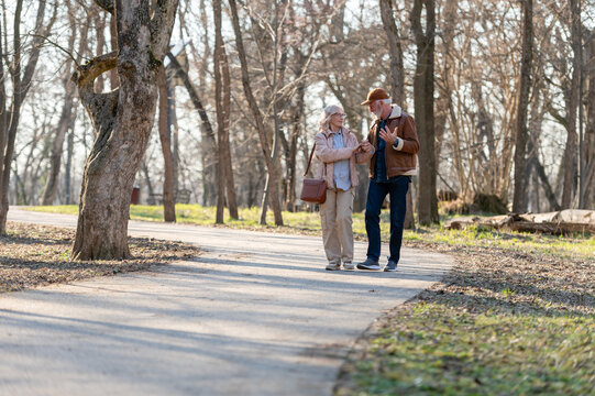 Cheerful senior couple enjoying a walk together in a sunlit park, holding hands and talking while maintaining an active, healthy and socially connected retirement lifestyle