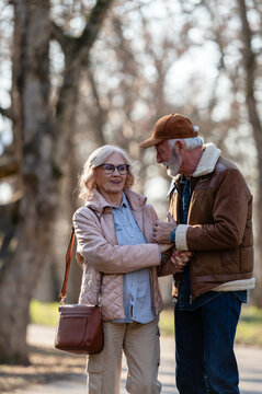 Smiling senior couple holding hands and enjoying a friendly conversation while strolling through a park, reflecting emotional connection, trust and a supportive relationship