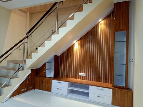 modern staircase with glass railings and wooden paneling. white cabinets and drawers below offer storage and style. warm lighting highlights the vertical wood grain design
