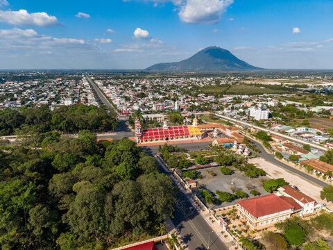 Aerial view of Tay Ninh Holy See Temple, a vibrant Cao Dai religious site with distinctive architecture, surrounded by lush trees and the urban landscape of Tay Ninh Hoa, Tay Ninh, Vietnam.