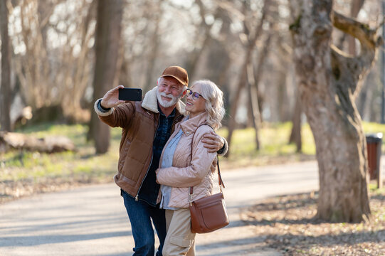 Happy retired couple taking a selfie together during an outdoor walk, enjoying nature, photography and shared experiences in a peaceful park