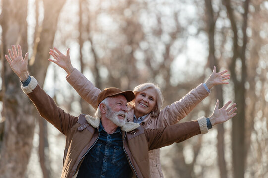 Joyful senior couple stretching their arms and holding hands in a sunlit park, expressing freedom, happiness and the pleasure of spending retirement together