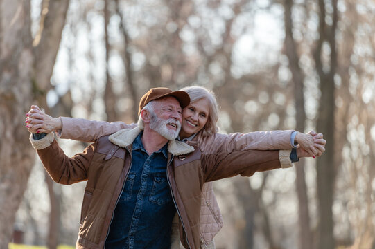 Romantic elderly couple smiling at each other while holding hands and playfully dancing in a park, celebrating lasting love, affection and happiness in later life