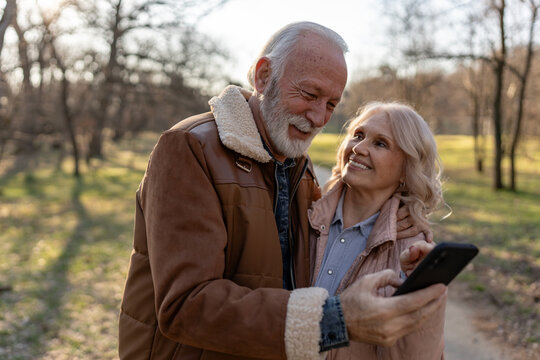 Loving senior couple embracing and smiling while sharing a smartphone outdoors, expressing affection, happiness and companionship in their later years
