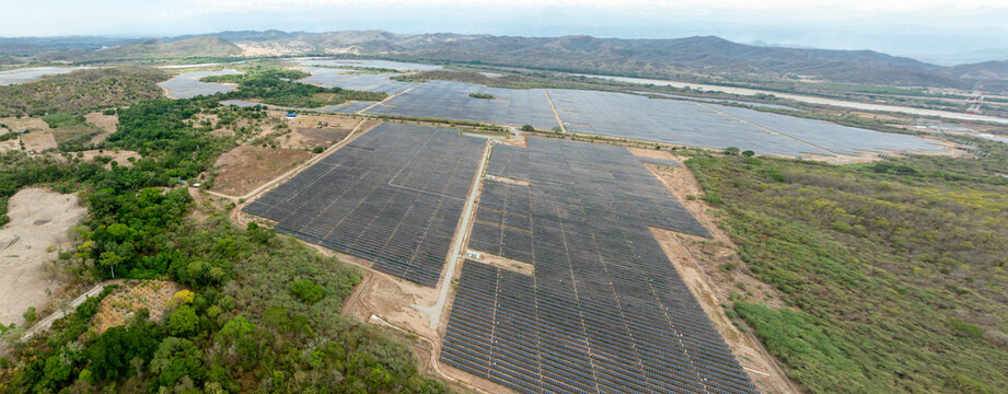 Aerial view of the Puerta de Oro solar photovoltaic park featuring massive arrays of solar panels set within a rural landscape with rolling hills in Guaduas, Cundinamarca, Colombia.