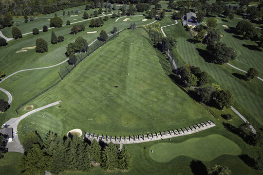 Aerial view of a golf course driving range with manicured green grass, practice bays, sand traps, and surrounding trees in Glenview, Illinois, United States.