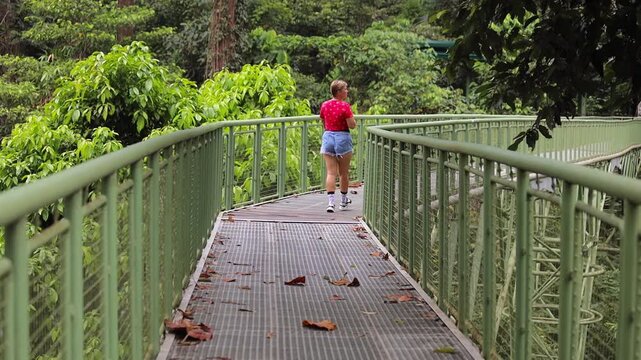 A person standing on a wooden canopy walkway surrounded by lush green rainforest in Sandakan, Borneo, Malaysia, enjoying the tropical jungle views