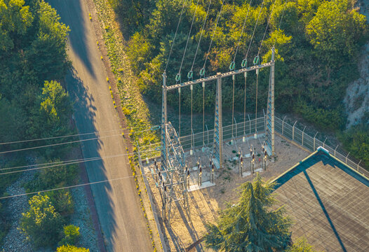 Aerial view of high voltage electrical substation and power transmission lines surrounded by dense forest and a paved road, France.