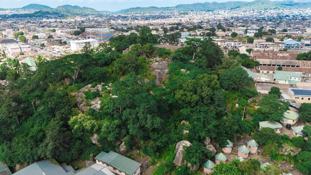 Aerial view of Jos Wildlife Park featuring lush green trees, rocky outcrops, and small buildings with the city of Jos in the background, Jos, Plateau, Nigeria.