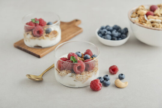 Yogurt dessert with granola and fresh raspberries and blueberries in a glass, served with a spoon