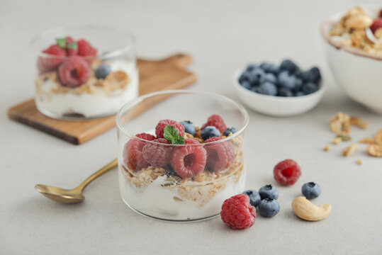 Yogurt dessert with granola and fresh raspberries and blueberries in a glass, served with a spoon