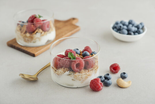 Yogurt dessert with granola and fresh raspberries and blueberries in a glass, served with a spoon