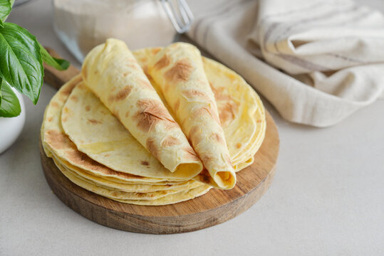 Stack of lavash or chapati flatbreads on a wooden cutting board, with a jar of flour, fresh basil