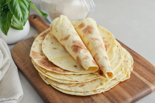 Stack of lavash or chapati flatbreads on a wooden cutting board, with a jar of flour, fresh basil