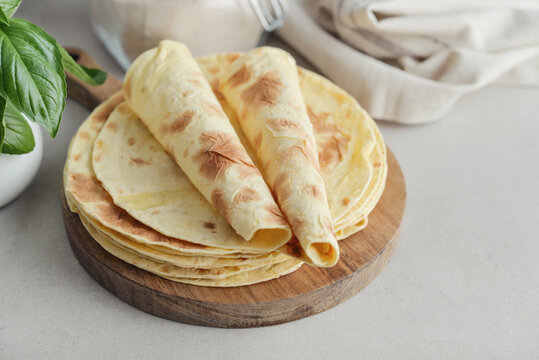Stack of lavash or chapati flatbreads on a wooden cutting board, with a jar of flour, fresh basil
