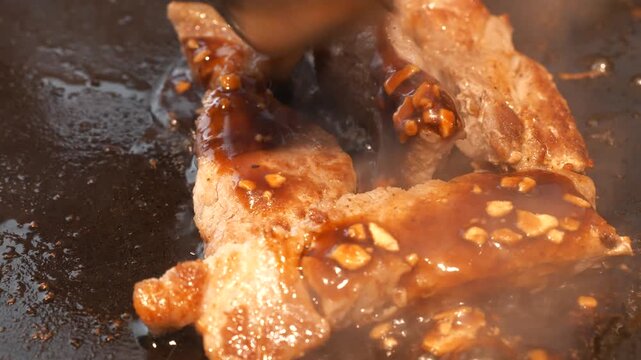 鉄板で焼いた豚ロースステーキにニンニク醤油ソースをかける仕上げの調理シーン、湯気とシズル感
