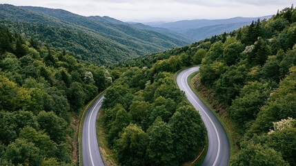 Fototapeta premium Aerial view of a winding two-lane asphalt highway curving through a dense forested valley surrounded by mountains